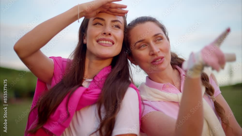 Two women dressed in white and pink clothes, holding golf clubs and talking on the course Two women dressed in white and pink clothes, holding golf clubs and talking on the course
