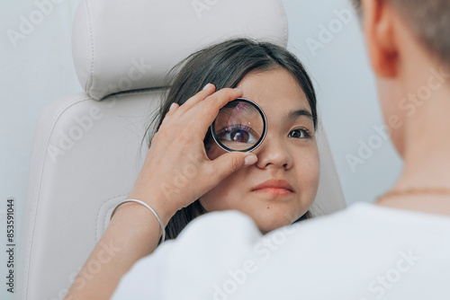 Doctor using magnifying glass to examine eye of girl at clinic photo