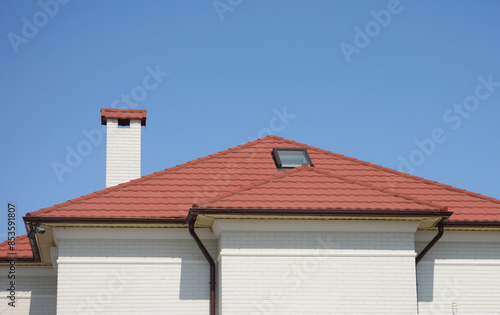 House attic rooftop with red clay tiles, skylight window, chimney, soffits, rain gutter pipeline, security camera.