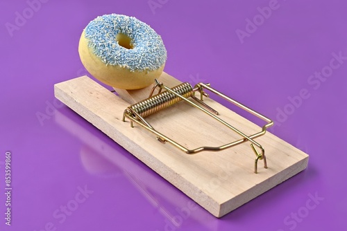 Delicious donut on wooden mousetrap isolated on purple.  Unhealthy eating concept. 