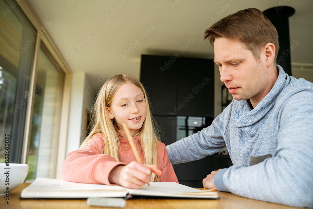 Father looking at daughter doing homework at table Father looking at daughter doing homework at table