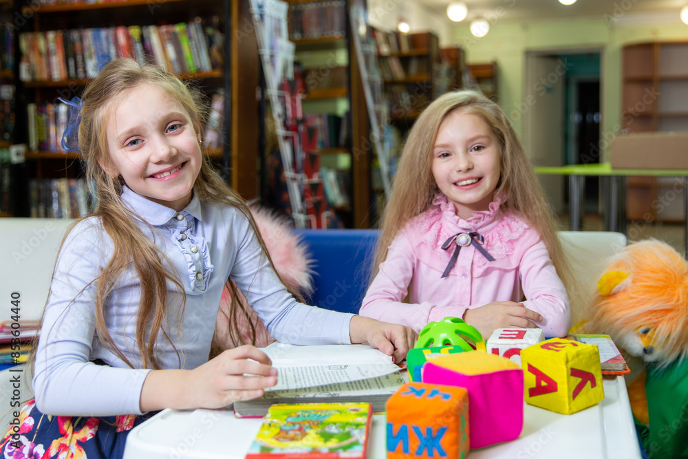 Two funny girls are reading books in the library. Wooden alphabet blocks Two funny girls are reading books in the library. Wooden alphabet blocks