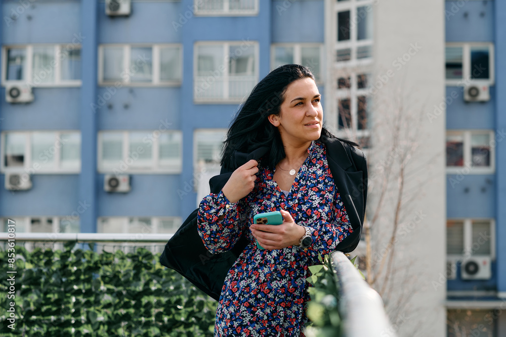 Fototapeta premium Businesswoman in Black Suit Using Smartphone on Break in Modern Urban Environment.