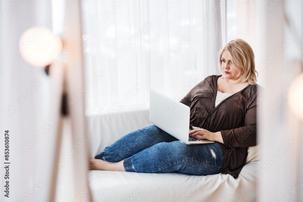 Overweight woman working on laptop from homeoffice, sitting on sofa with legs up. Overweight woman working on laptop from homeoffice, sitting on sofa with legs up.
