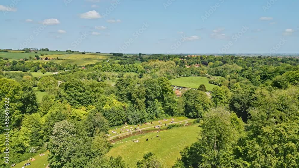 Drone-shot video of a British summer park—individuals having fun by a meandering stream, appealing picnic areas Drone-shot video of a British summer park—individuals having fun by a meandering stream, appealing picnic areas