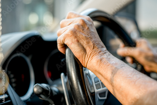 A senior man is driving a car with his hand on the steering wheel photo