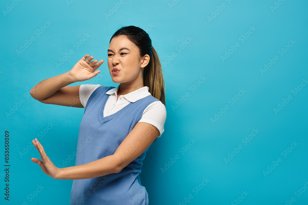 A young Asian woman in smart casual attire stands against a blue background, her expression suggesting a mix of disgust and disbelief. A young Asian woman in smart casual attire stands against a blue background, her expression suggesting a mix of disgust and disbelief.