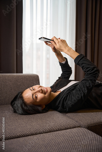 Happy successful lady resting on sofa holding phone in hands