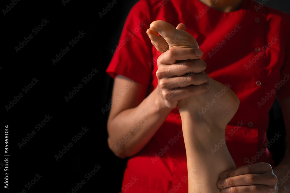 Close-up of a masseur in a red uniform doing foot massage to a young woman, copy space. Foot massage at the spa. Foot care.