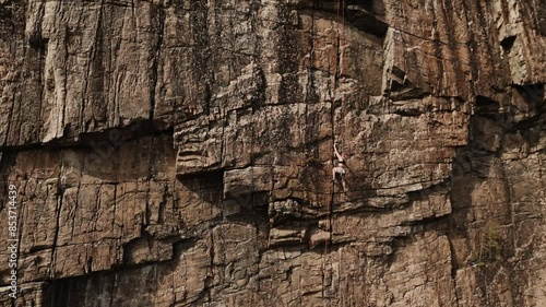 Powerful woman climbing extremely dangerous rock wall, aerial view