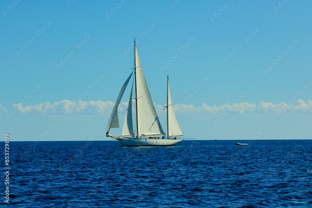 Fototapeta premium A sailboat is sailing in the ocean with a clear blue sky in the background