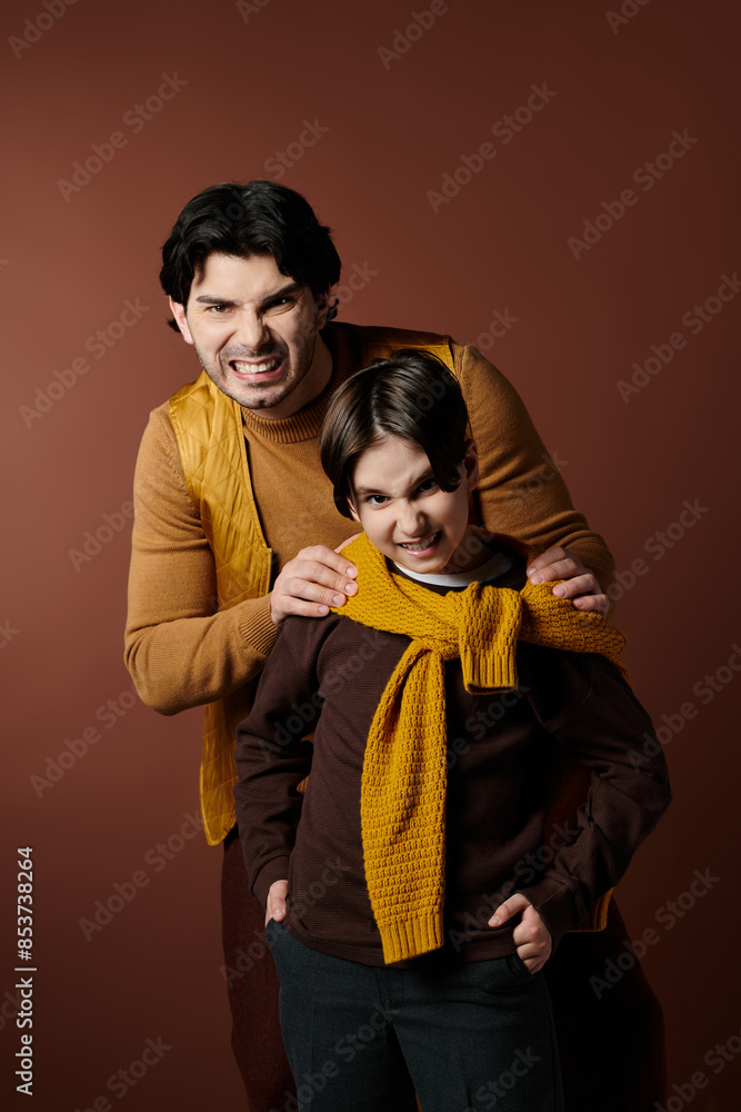 Fototapeta premium A father and son stand close together, both with playful expressions on their faces.