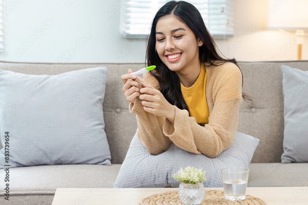 Young Woman Smiling While Holding Pregnancy Test in Cozy Living Room Setting, Celebrating Positive Result Young Woman Smiling While Holding Pregnancy Test in Cozy Living Room Setting, Celebrating Positive Result
