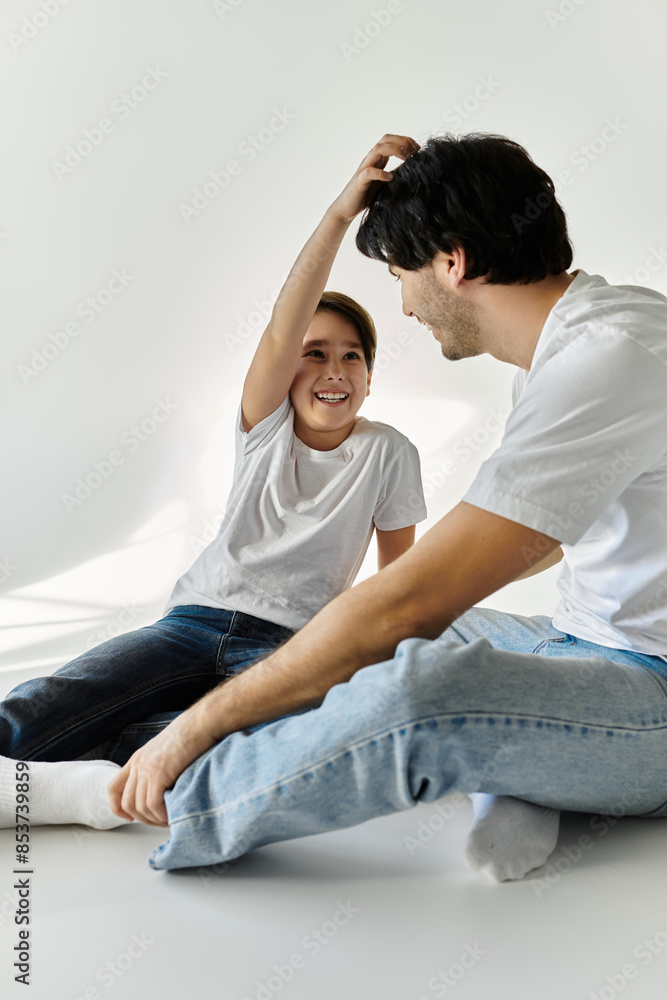Obraz premium A father and his son are sitting on the floor in a white room, laughing and playing together.