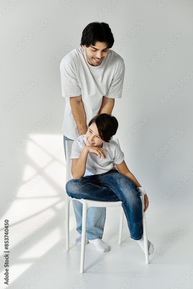 A father smiles down at his son who is sitting on a white chair. A father smiles down at his son who is sitting on a white chair.