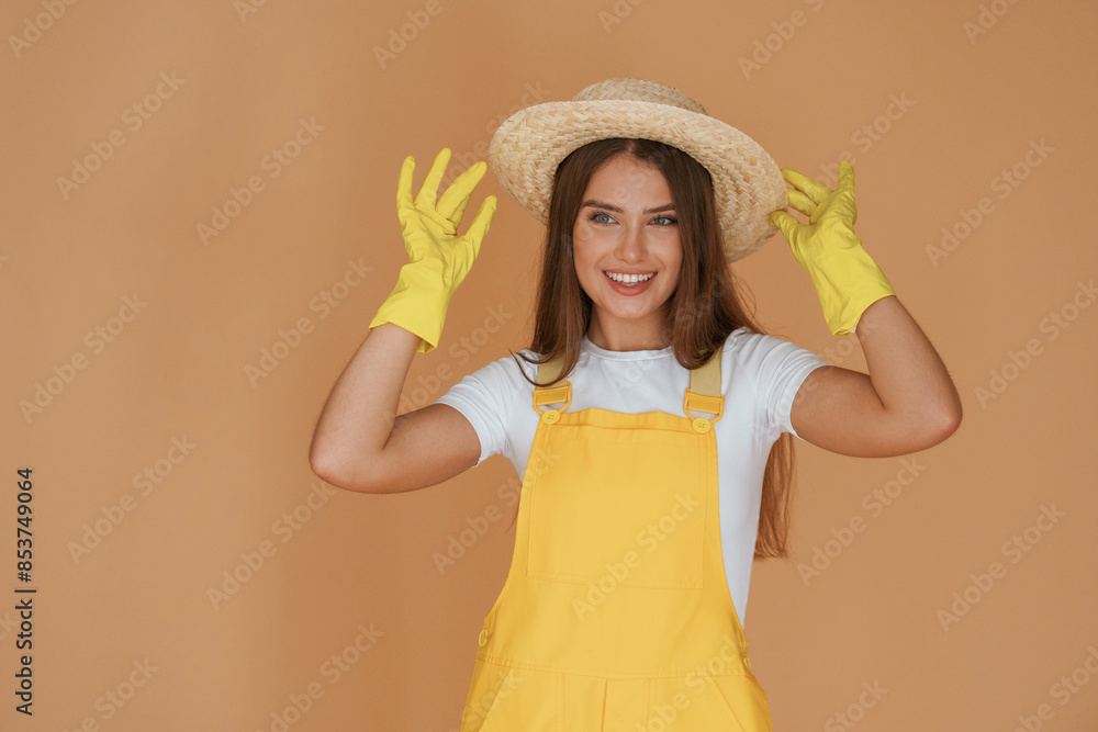 Garden worker is in straw hat. Young pretty woman is against background in the studio Garden worker is in straw hat. Young pretty woman is against background in the studio