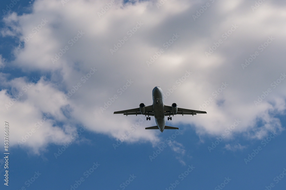 Unmarked passenger plane flying low with white clouds and a blue sky in the background Unmarked passenger plane flying low with white clouds and a blue sky in the background
