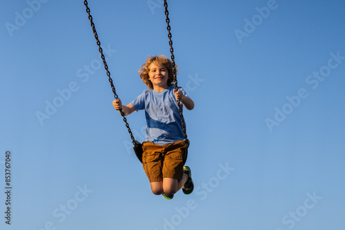 Child extreme swinging. Danger high Swing in sky. Cute child having fun on a swing on summer sky background. Blonde little boy swings at kid playground. Child swinging high.