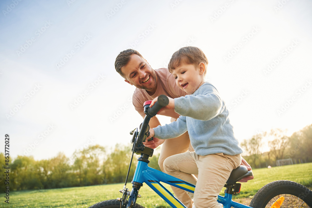 Trying the bicycle. Happy father with son are having fun on the field at summertime