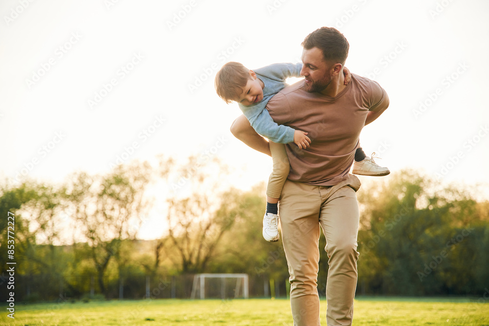 Wellbeing, kid is on the shoulders or back. Happy father with son are having fun on the field at summertime Wellbeing, kid is on the shoulders or back. Happy father with son are having fun on the field at summertime