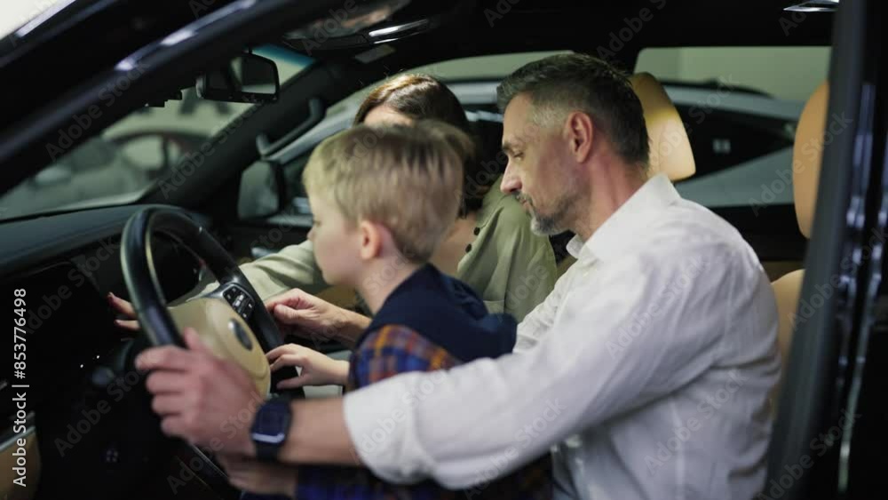 A middle-aged man with gray hair in a white shirt along with his wife and little blond son with blue eyes are sitting in the interior of a modern car during their trip to a car dealership