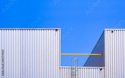 Aluminium corrugated steel wall of 2 industrial factory buildings with cylinder ladder and metal pipeline system against blue clear sky background © Prapat