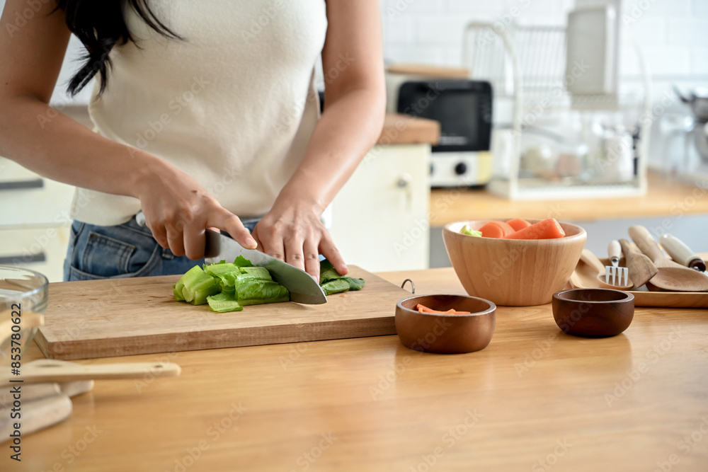 A close-up image of a woman cutting lettuces on a cutting board at a wooden kitchen tabletop, cooking in the kitchen. healthy food, lifestyle, home cooking A close-up image of a woman cutting lettuces on a cutting board at a wooden kitchen tabletop, cooking in the kitchen. healthy food, lifestyle, home cooking