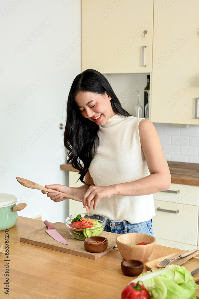 An attractive Asian woman is in the kitchen, holding a bowl of salad and a wooden spatula, enjoying cooking in the kitchen. home cooking and healthy eating life concepts An attractive Asian woman is in the kitchen, holding a bowl of salad and a wooden spatula, enjoying cooking in the kitchen. home cooking and healthy eating life concepts