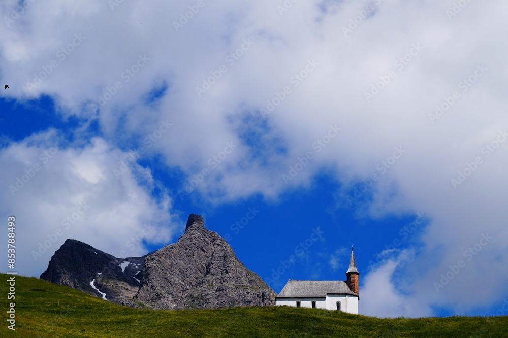 St. Jakob Chapel on Simmel next to the mountain, against the background of blue sky and white clouds. Hochtann Mountain Pass, Vorarlberg, Austria St. Jakob Chapel on Simmel next to the mountain, against the background of blue sky and white clouds. Hochtann Mountain Pass, Vorarlberg, Austria