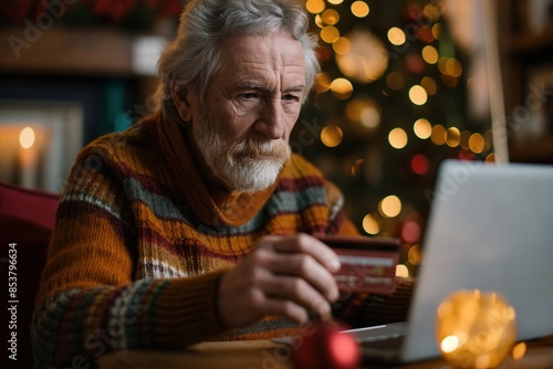 Close up photo of a senior man holding a credit card while using a laptop, possibly for online shopping or banking services, 