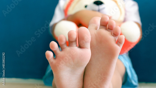 Asian young girl sitting on the floor, hugging the white doll. Closeup the bare feet.