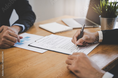 Fototapeta Naklejka Na Ścianę i Meble -  businessman sitting at desk holds pen signing contract paper, lease mortgage, employment hr or affirm partnership
