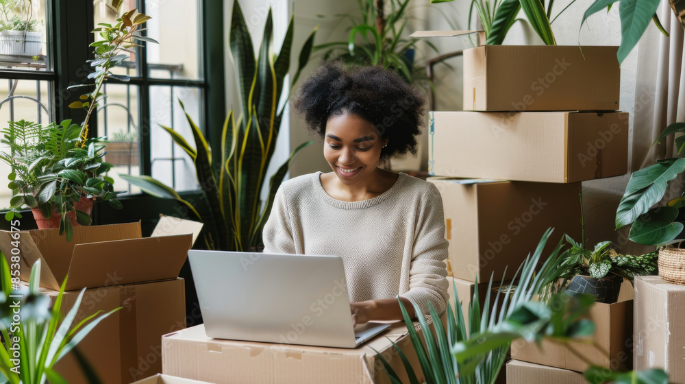 A woman with a bright smile works on her laptop, surrounded by lush green plants and cardboard boxes, suggesting a recent move into a new, vibrant space. A woman with a bright smile works on her laptop, surrounded by lush green plants and cardboard boxes, suggesting a recent move into a new, vibrant space.