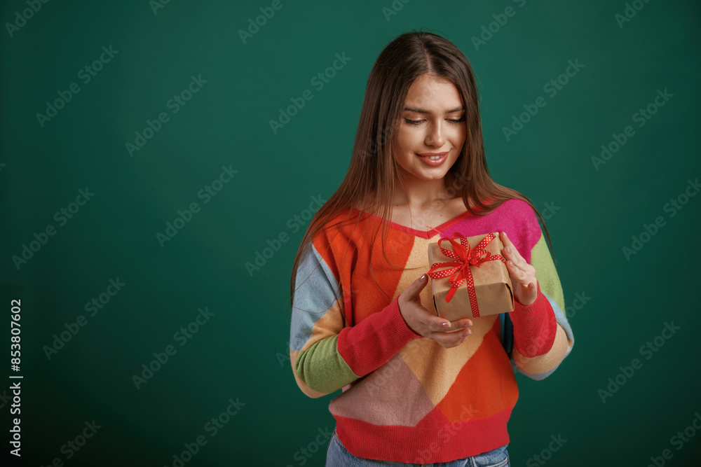Little present in hands. Gift box. Young woman is standing against green background in the studio Little present in hands. Gift box. Young woman is standing against green background in the studio