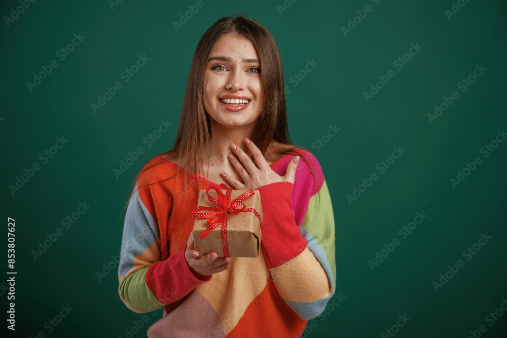 Thankful, holding little gift box. Young woman is standing against green background in the studio Thankful, holding little gift box. Young woman is standing against green background in the studio