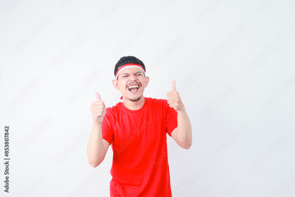 Smiling happy handsome young Asian man in casual t-shirt standing confident and gesturing thumbs up isolated over white background. Celebrate Indonesia independence day on 17 August Smiling happy handsome young Asian man in casual t-shirt standing confident and gesturing thumbs up isolated over white background. Celebrate Indonesia independence day on 17 August