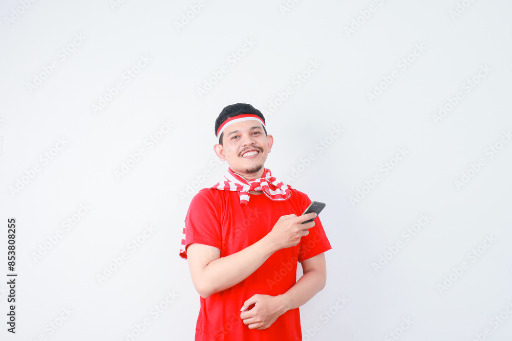 Excited young Asian man in casual t-shirt using mobile phone, getting good news isolated on grey background. indonesian independence day celebration concept Excited young Asian man in casual t-shirt using mobile phone, getting good news isolated on grey background. indonesian independence day celebration concept