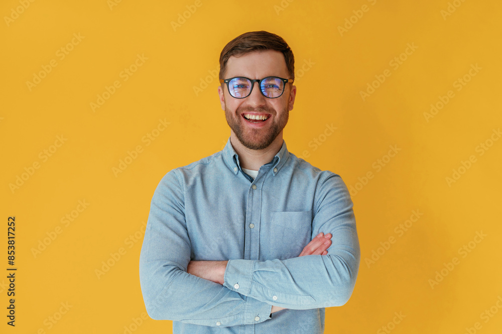 Standing with arms crossed. Attractive man in blue shirt is against yellow background