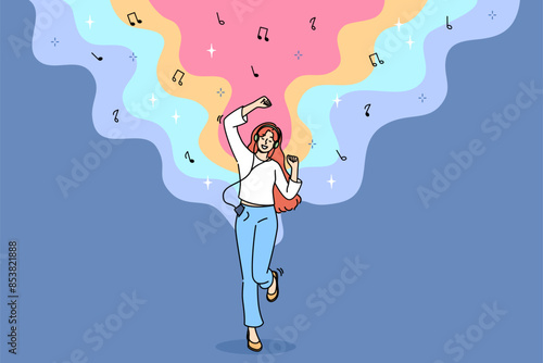 Teenage woman listens to music on headphones and dances rhythmically with hands, and uses phone with wired headset. Energetic girl with music player enjoys latest album of favorite rock band