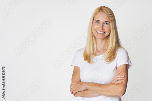 Canvastavla A smiling blonde woman with long hair is wearing a white t-shirt and has her arms crossed in front of her