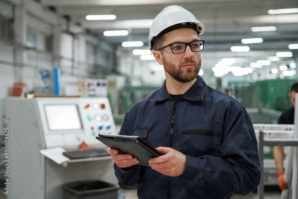 Holding tablet. Factory worker is indoors with hard hat Holding tablet. Factory worker is indoors with hard hat