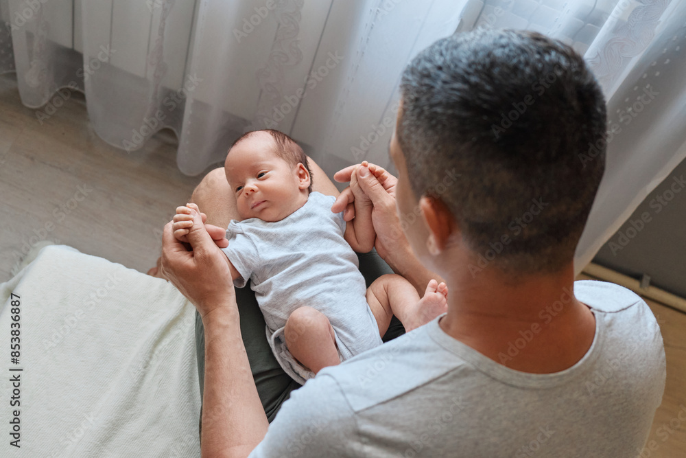 Anonymous father holding his newborn baby in home interior affectionately interacting with his baby gently rocking his newborn Anonymous father holding his newborn baby in home interior affectionately interacting with his baby gently rocking his newborn