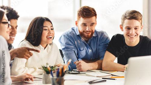 Team of college students talking over group project, looking at laptop screen