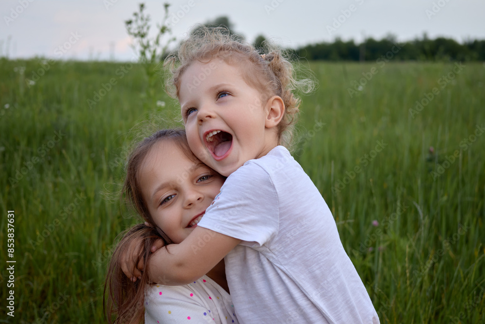 Funny Caucasian children girls sitting on field grass together in parks outdoors playing happily together in summer meadow expressing happiness and positive emotions Funny Caucasian children girls sitting on field grass together in parks outdoors playing happily together in summer meadow expressing happiness and positive emotions