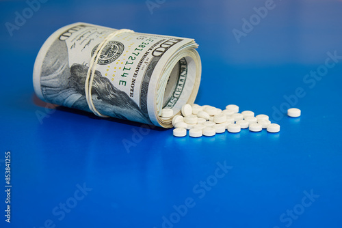 A rolled up wad of hundred dollar bills with white pills spilling out of it onto the table, money for medical treatment, expensive drugs, plantation medicinea photo