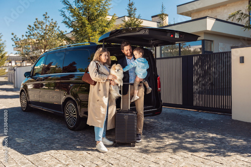 A young stylish family with their son and dog, stands near taxi trunk with luggage