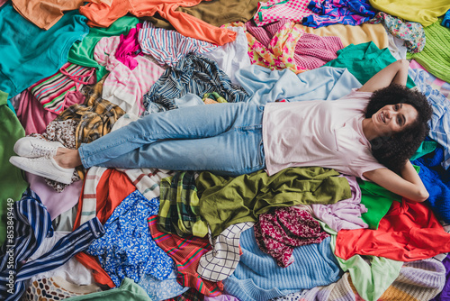 Full size above view photo of young woman laying messy pile stack clothes apartment indoors