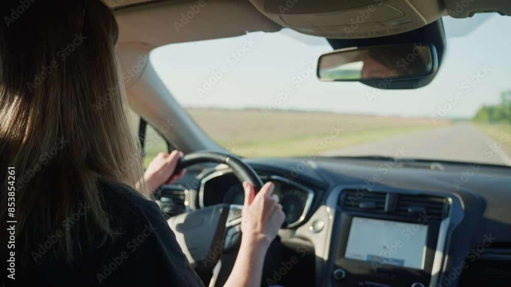 Woman driving car on country road at sunset. Back view of female driver in vehicle