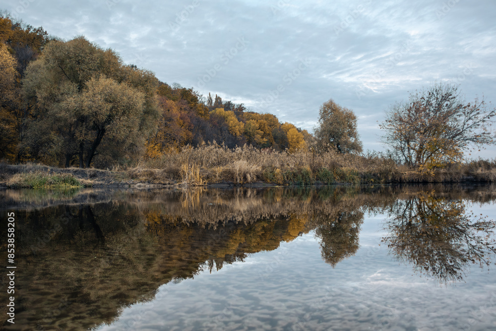 River scenery with autumn trees and clouds reflecting in mirror calm water surface