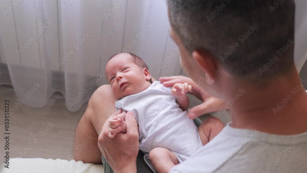 Devoted father holding his newborn baby in home interior gazing at his child with love affectionately interacting with his baby during first days of child life Devoted father holding his newborn baby in home interior gazing at his child with love affectionately interacting with his baby during first days of child life